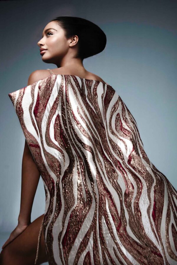 Luxury couture gown with rose-toned brocade fabric, dramatic side slits, and a sculptural back design.